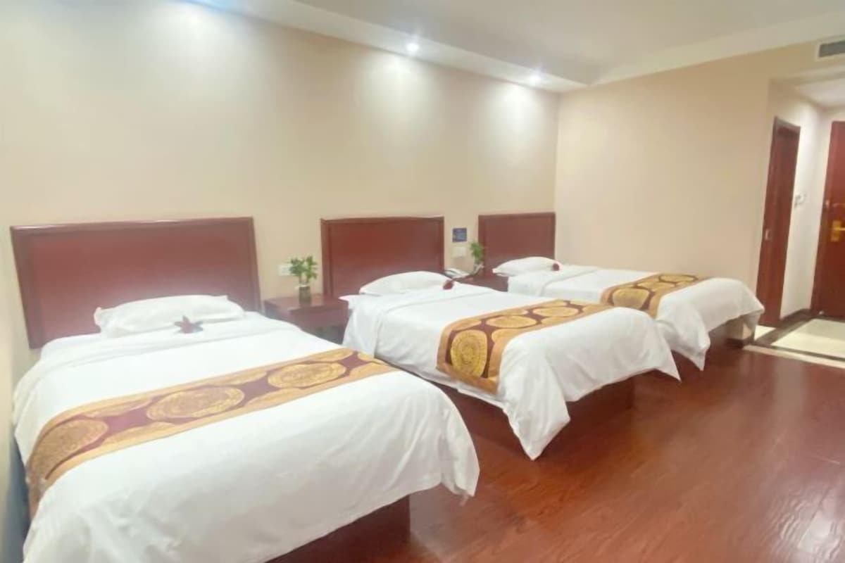 A hotel room with three single beds, wooden headboards, white bedding, and a wooden floor.
