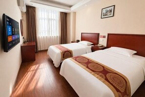 A hotel room with two beds, a TV, a desk, and a window with curtains.