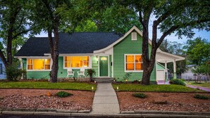 Une maison verte avec un toit foncé, un porche à l’avant et une allée menant à l’entrée.