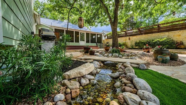 Un jardin avec un petit ruisseau, des rochers et des plantes en pot.