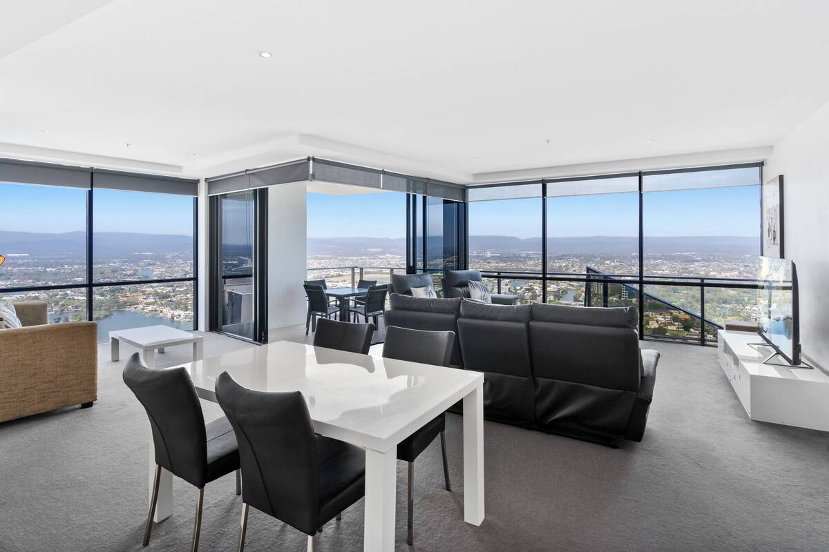 A modern, spacious balcony with a panoramic city view, a dining area with a glass table, and comfortable seating.