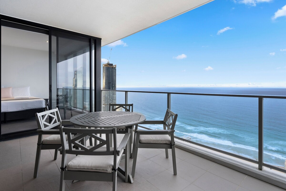 A balcony with a table and chairs, overlooking a body of water and a city skyline.