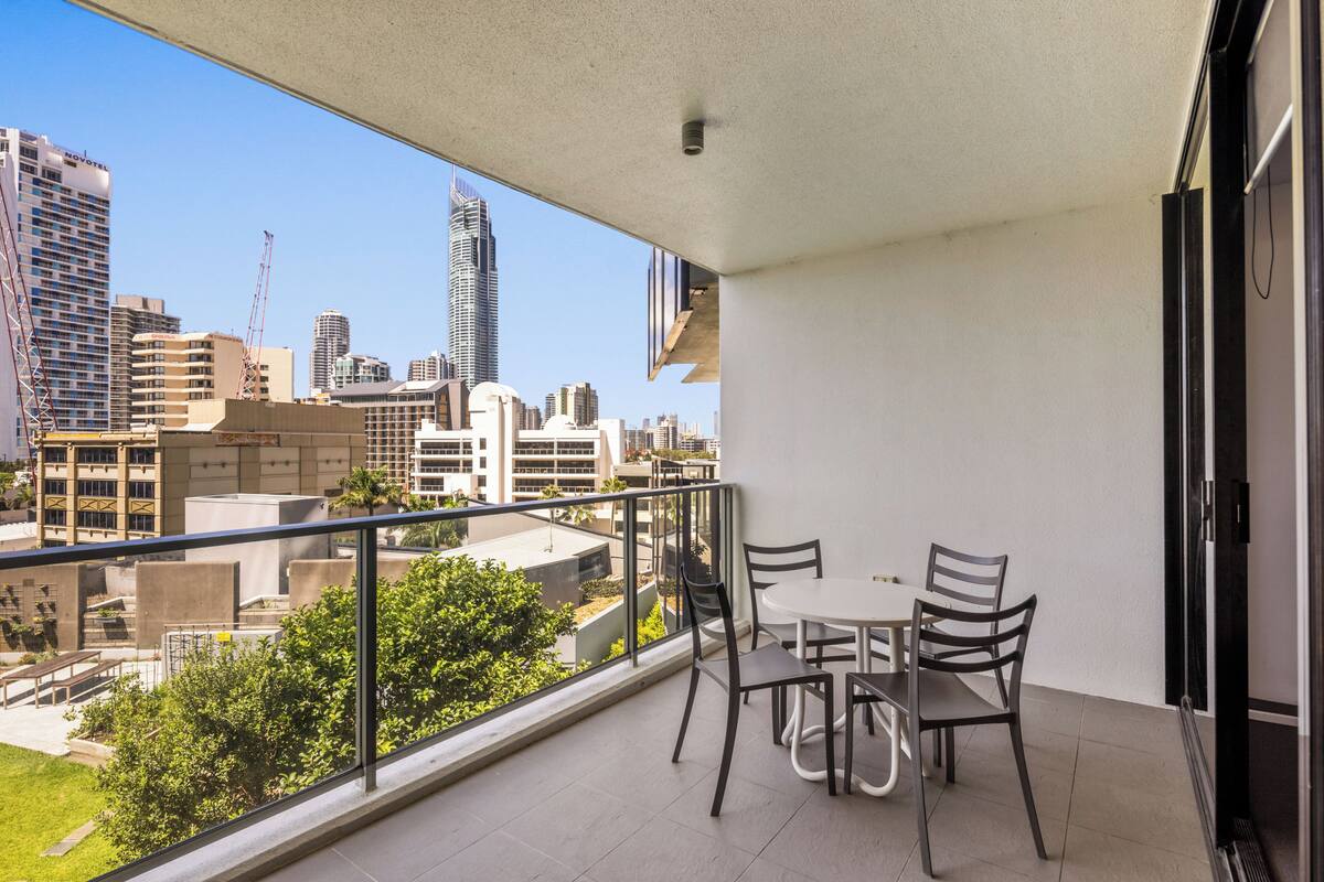 A balcony with a table and chairs, overlooking a cityscape with various buildings.