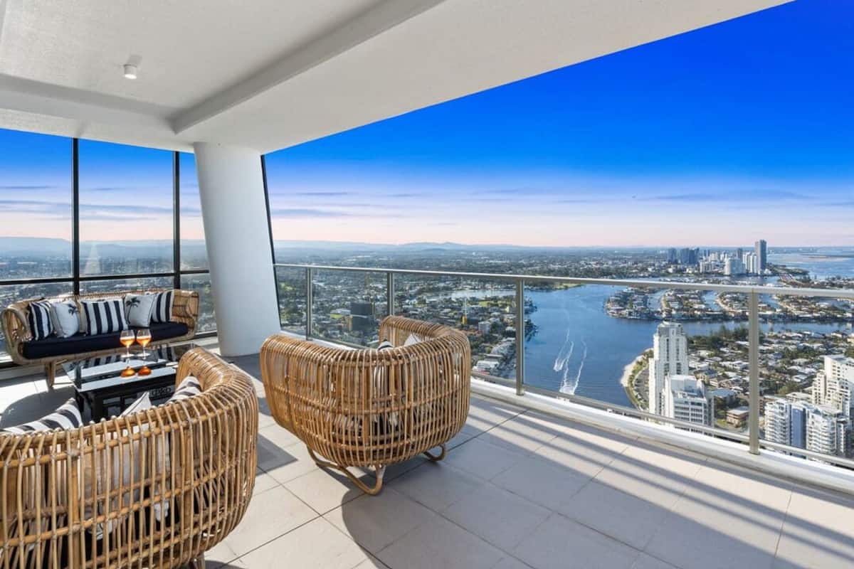 A balcony with wicker furniture, a glass table, and a city view.