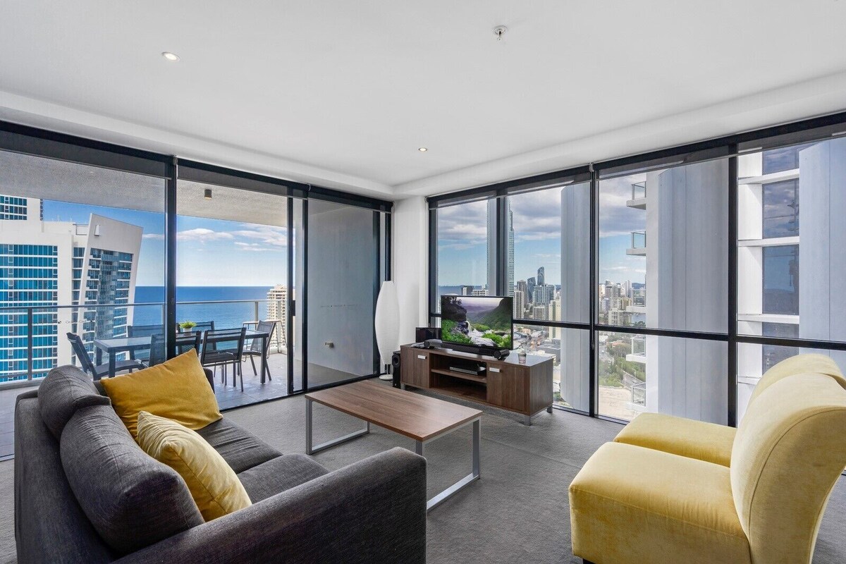 A modern living room with a large window, a flat-screen TV, a coffee table, and two sofas.
