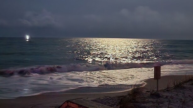 Eine Nachttagesszene am Strand mit hellem Mond und einer entfernten Lichtquelle.