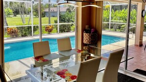 Un espace repas moderne avec une table et des chaises en verre, une vue sur une piscine et un panier contenant divers objets posé sur une table.