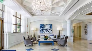 A spacious lobby with a chandelier, a large abstract painting, and a blue coffee table.