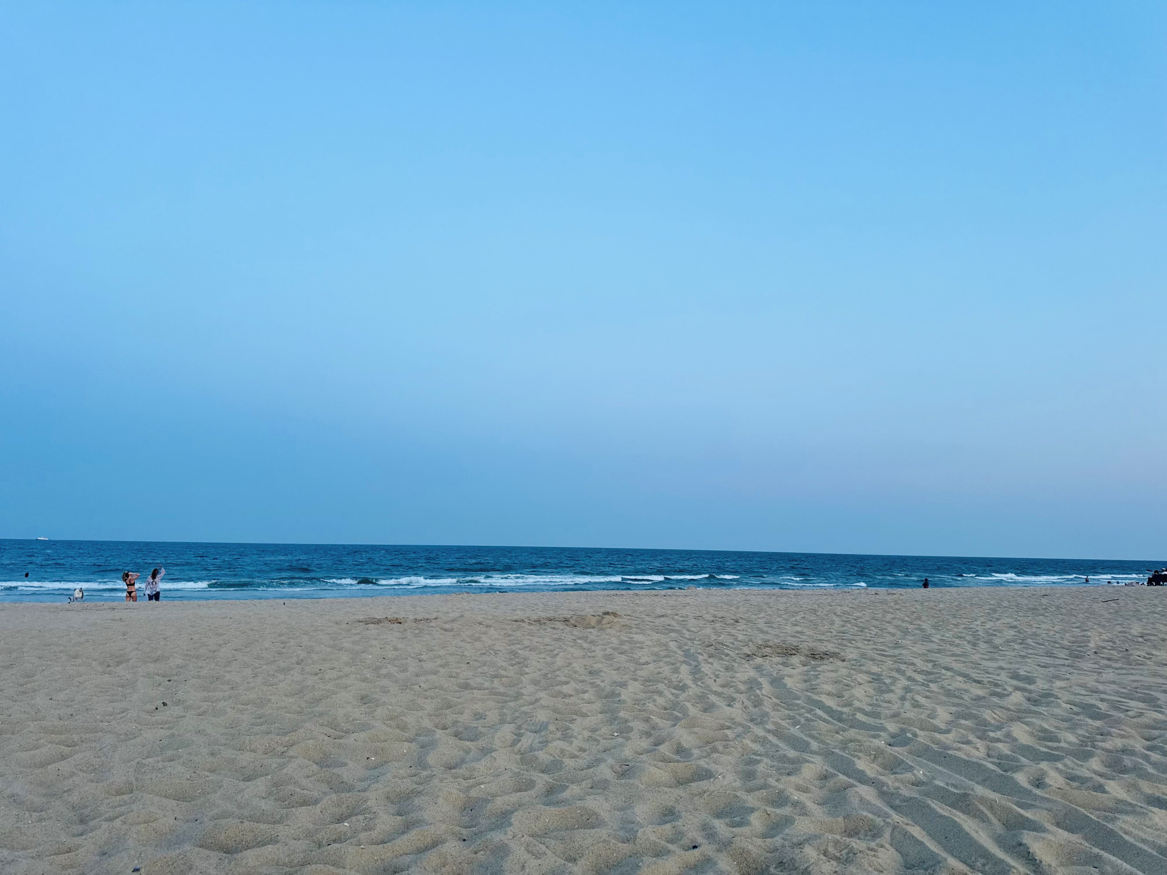A wide sandy beach with gentle waves and a clear sky.
