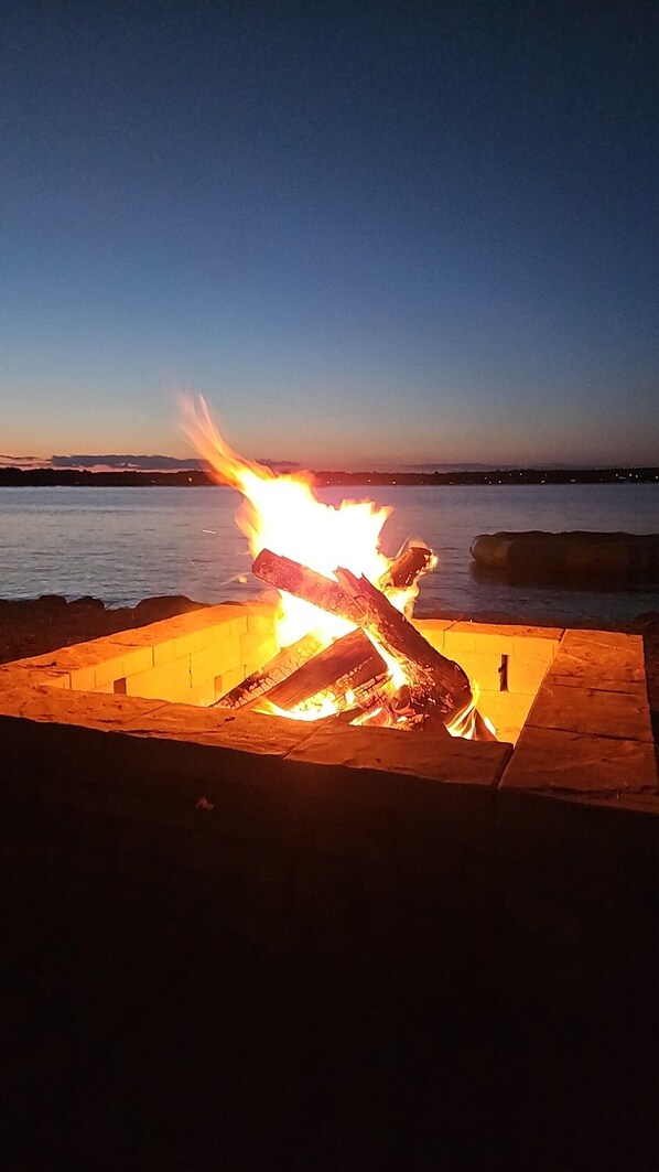 A campfire at dusk with a body of water in the background.