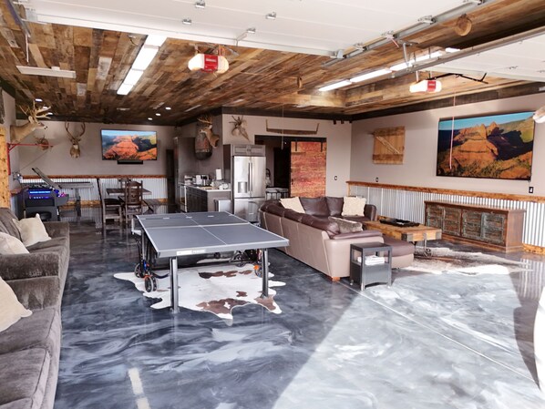 Amplia sala de estar con mesa de ping pong, sofá de cuero y techo rústico.
