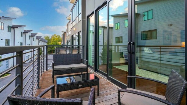 A balcony with wicker furniture, glass doors, and a view of neighboring buildings.