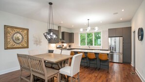 A modern kitchen with a dining area, wooden flooring, and a large window providing natural light.