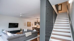 A modern living room with a grey sofa, a flat-screen TV, and a dining area in the background.