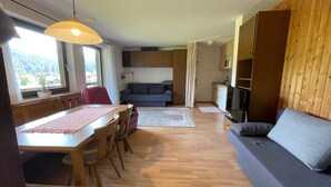 Un espace de vie compact comprenant un coin repas, un canapé, une kitchenette et une vue sur l’extérieur.