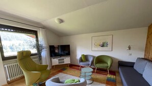 Una sala de estar con televisión, dos sillones, un sofá y una alfombra estampada.