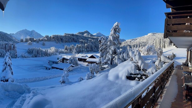 Un paisaje montañoso nevado con cielo despejado, un edificio de madera con balcón y árboles cubiertos de nieve.
