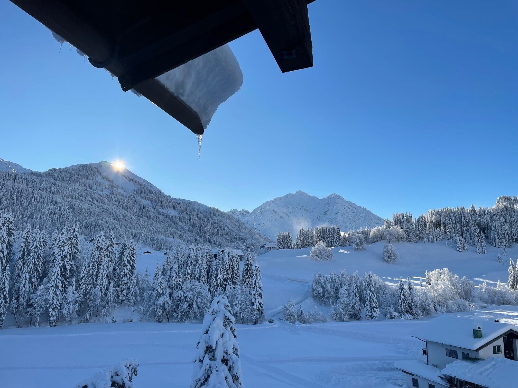 Paesaggio montuoso innevato con cielo sereno e una casa in primo piano.