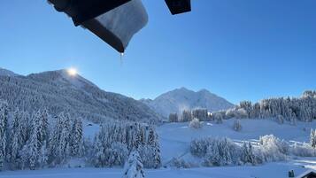 Paesaggio montuoso innevato con cielo sereno e una casa in primo piano.