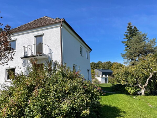 Ein weißes Gebäude mit Balkon, umgeben von Grünpflanzen und Bäumen.