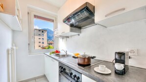 A modern kitchen with a stove, oven, sink, and a window with a view of buildings and mountains. - Casa Rosa with Balcony in Lugano, Lugano, Switzerland (Lugano)