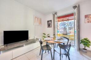 A modern living room with a flat-screen TV, a dining table with chairs, a potted plant, and a balcony with a view. - Casa Rosa with Balcony in Lugano, Lugano, Switzerland (Lugano)