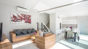 A modern living room with a sofa, coffee table, and artwork. There is a staircase leading to an upper level. - Elegant Designer 4BR Pool Villa Skylight (Kamala)