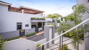 A modern residential building with a covered outdoor area, a car parked in front, and a staircase leading to an upper level. - Elegant Designer 4BR Pool Villa Skylight (Kamala)