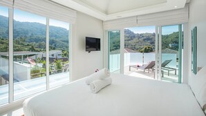 A spacious bedroom with a large bed, a flat-screen TV mounted on the wall, and a balcony with a view of lush greenery and a pool. - Elegant Designer 4BR Pool Villa Skylight (Kamala)