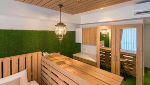Une pièce avec un banc en bois, une petite table et un mur vert. On y trouve un luminaire suspendu et un meuble en bois doté de portes en verre.