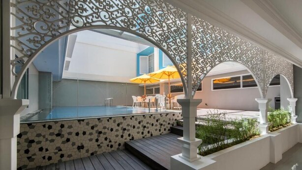 Un espace piscine doté d’une terrasse carrelée, de colonnes blanches et de coins salon extérieurs abrités sous une marquise décorative.