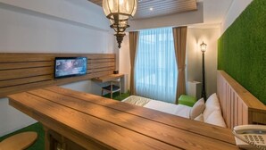 Une chambre d’hôtel avec un bureau en bois, une télévision, un mur vert et une moquette verte.