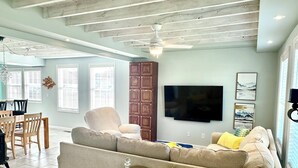 Un salon comprenant un canapé, une table basse en verre, un téléviseur fixé au mur et un ventilateur de plafond.
