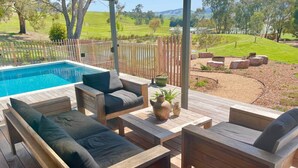 Eine Holzterrasse mit Gartenmöbeln, einem Pool und Blick auf eine grüne Landschaft.