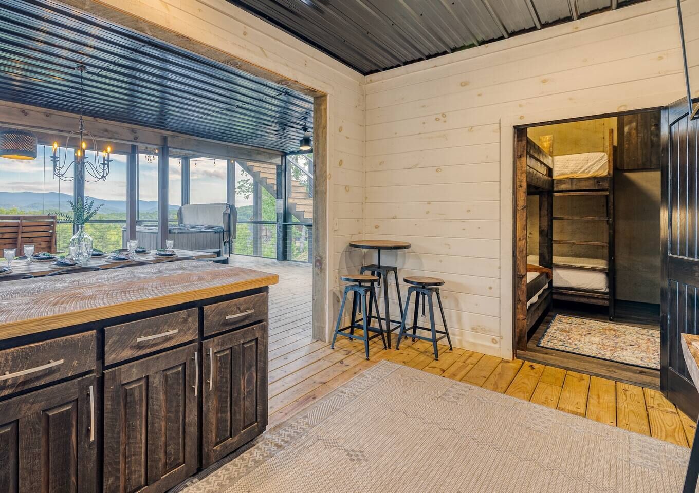 Ein rustikales Blockhaus-Interieur mit einem Holzesstisch, Barhocker, einem Etagenbett und einem großen Fenster mit schöner Aussicht.