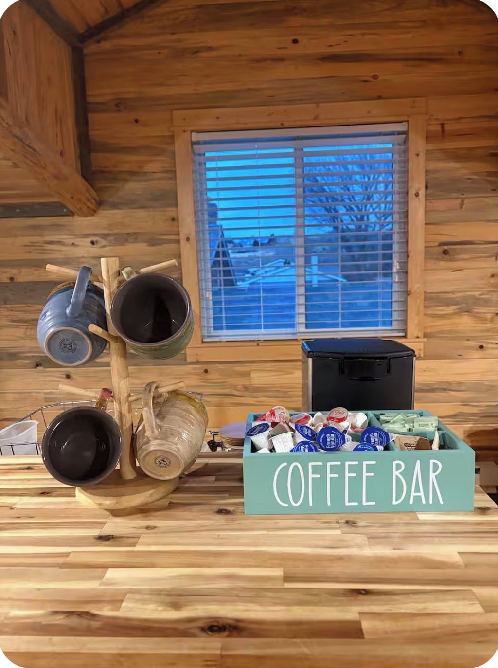 Interior de madera con una barra de café, que incluye tazas, una tetera y un letrero que dice 'COFFEE BAR'.