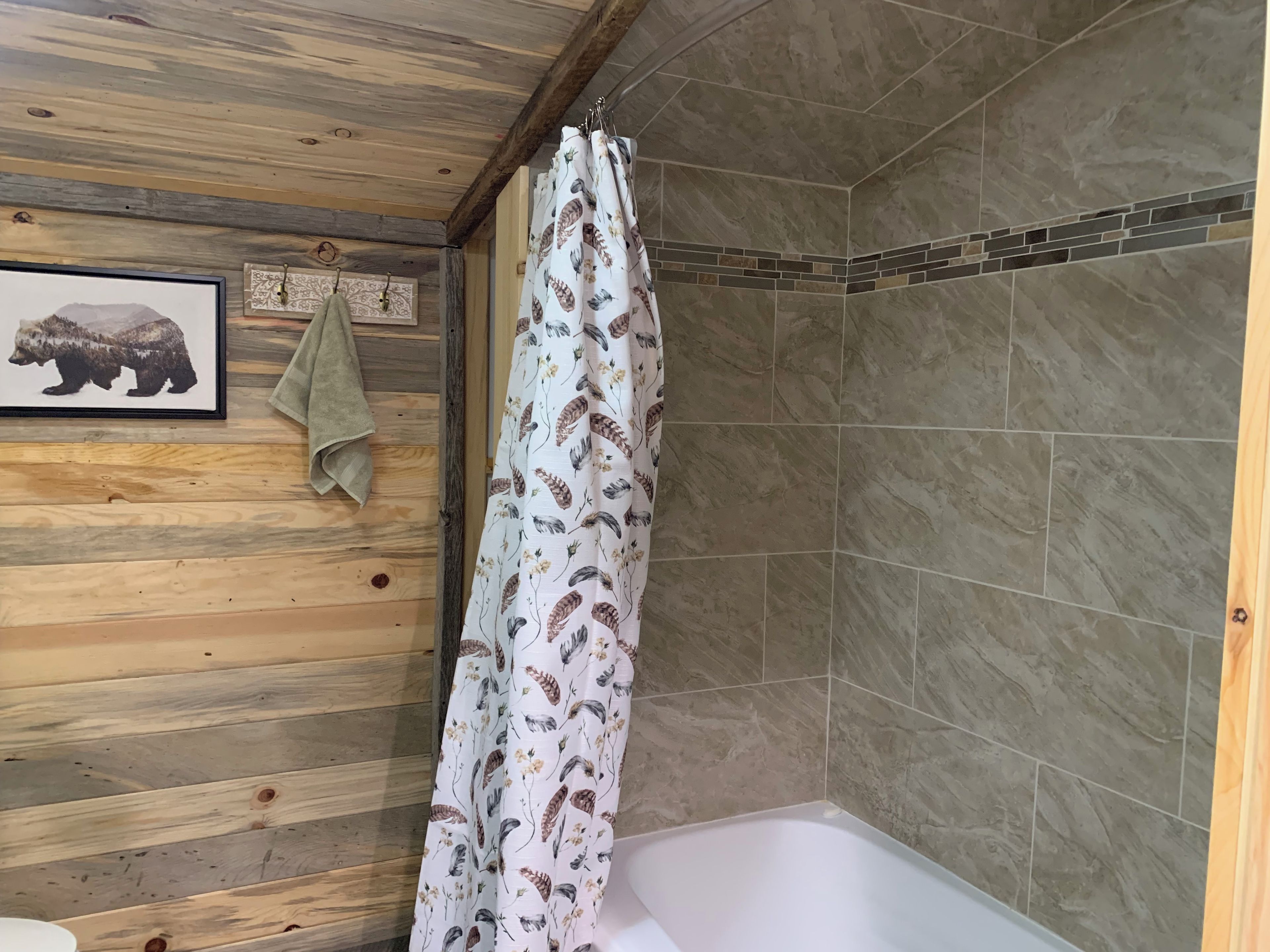 Casa de banho com teto de madeira, cortina de chuveiro estampada com pássaros, quadro com animais e toalha na parede.