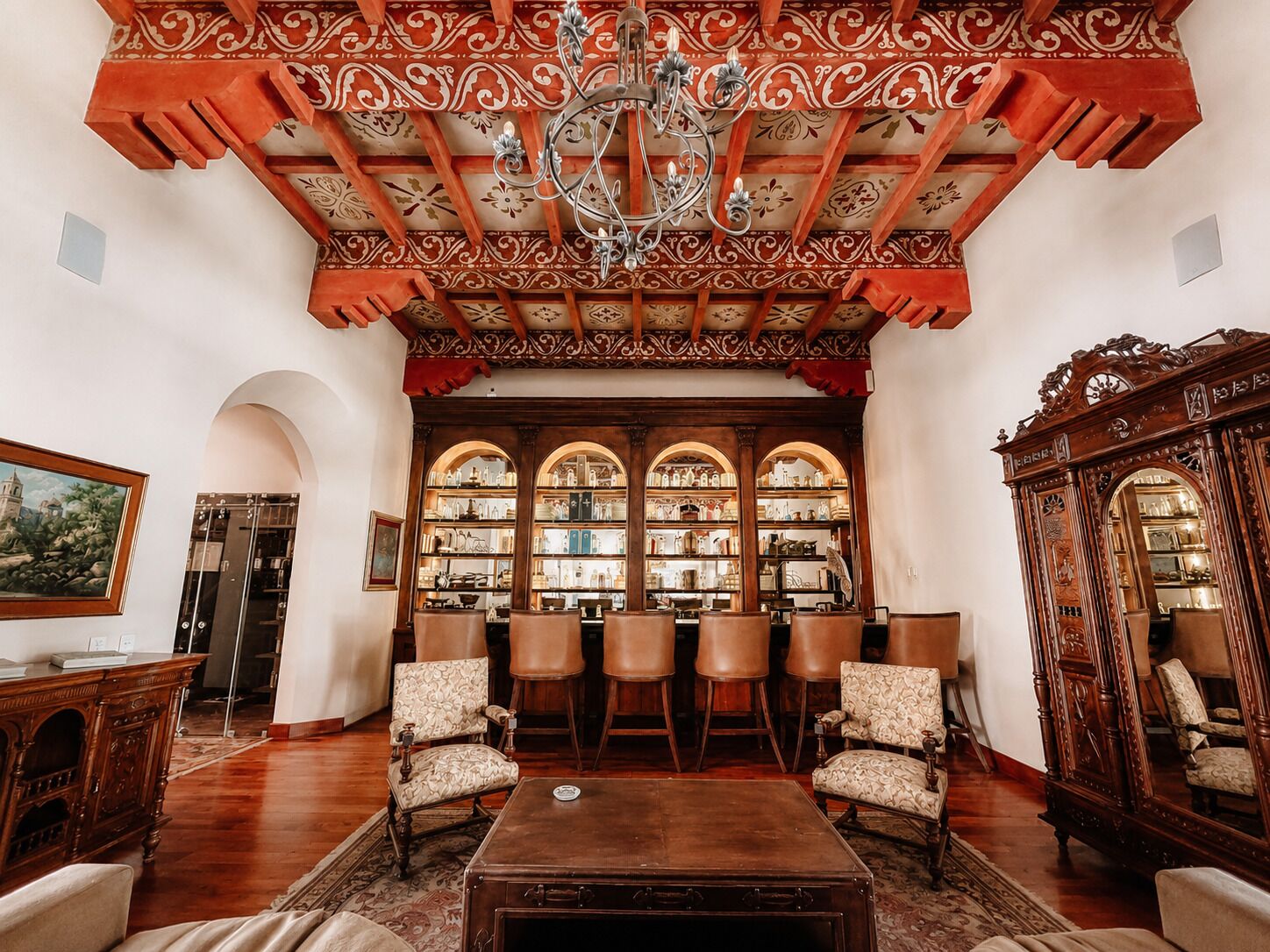 Una habitación espaciosa con techo alto, ornamentado de madera, un candelabro y un gran ventanal en arco.