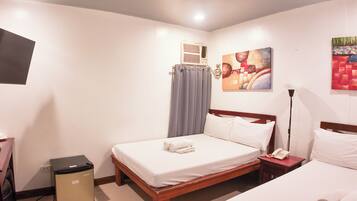 A hotel room with a single bed, a bedside table with a lamp, a small trash bin, and a wall-mounted air conditioning unit.