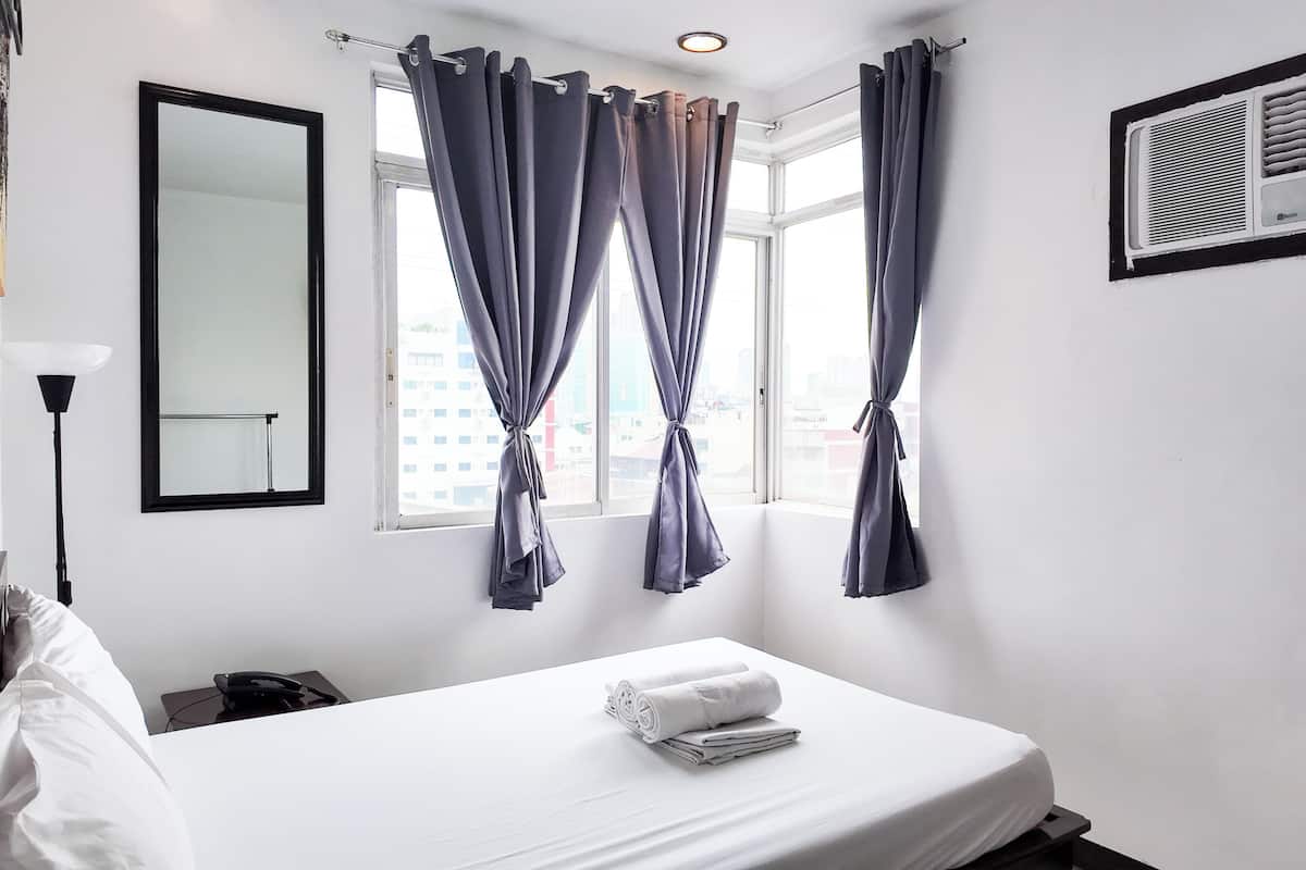 Habitación de hotel con cama, espejo, ventana con cortinas y aire acondicionado.