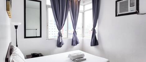 Une chambre d’hôtel équipée d’un lit, d’un miroir, d’une fenêtre avec des rideaux et d’un appareil de climatisation.