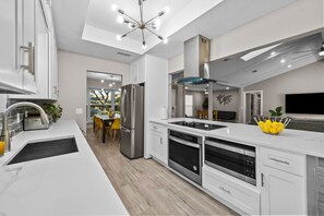 A modern kitchen with white cabinetry, stainless steel appliances, a black sink, and a dining area with yellow chairs. - Family Friendly, Heated Pool Spa, 2 King Beds, Cornhole, Foosball, Games, Grill (Richardson)