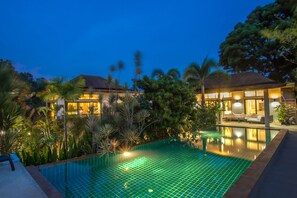 A swimming pool with a tiled edge, surrounded by lush greenery and palm trees. - Grand Tropical Pool Villa Oxavia NaiHarn (Rawai)