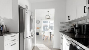 A modern kitchen with stainless steel appliances, white cabinetry, and a geometric backsplash. - Luxury MCM King Suite • Coffee Lover's Dream! • EV2 (Salem)