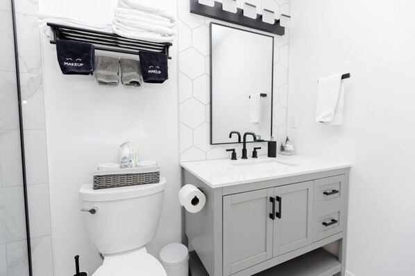 Uma casa de banho moderna com sanita, lavatório e toucador. Existem toalhas e produtos de higiene pessoal no balcão do lavatório.