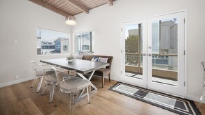 Un espace repas doté d’un plafond en bois, d’une grande fenêtre, d’une table à manger avec des chaises, d’un banc et d’une porte avec des panneaux de verre.