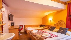 Una camera d'albergo con due letti singoli, una testiera in legno, un comodino con una lampada, una sedia rossa, una scrivania con un computer e un bagno con un lavandino.