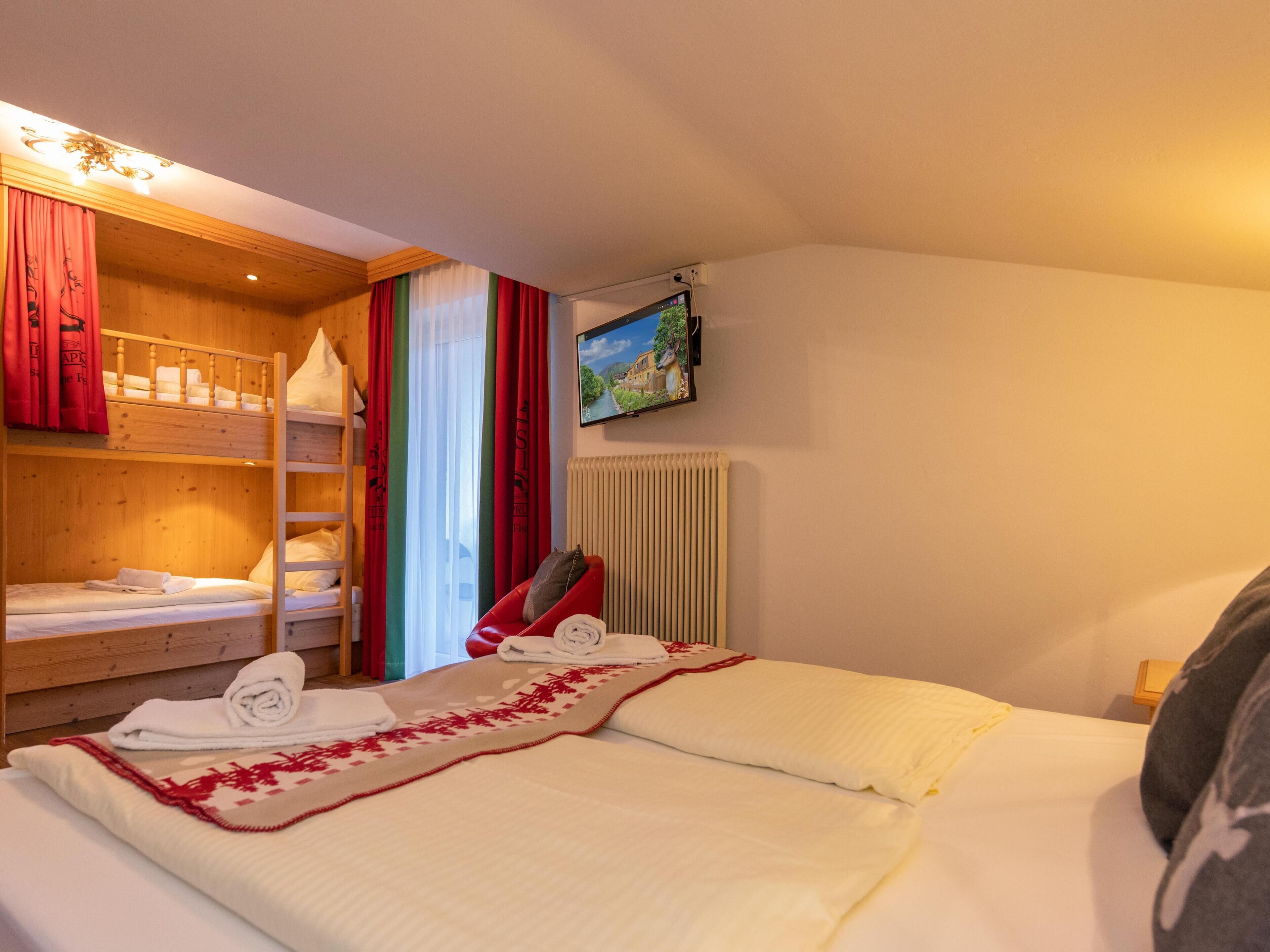 A hotel room with a bunk bed, a single bed, a radiator, and a TV on the wall.