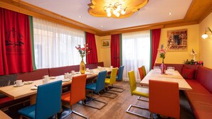 Zona pranzo con tavoli in legno, sedie colorate e tende rosse.