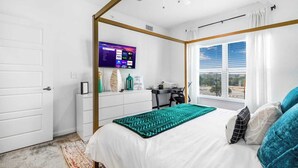 Ein Schlafzimmer mit einem Bett, einem Schreibtisch, einem Fernseher und einem Fenster mit Jalousien.